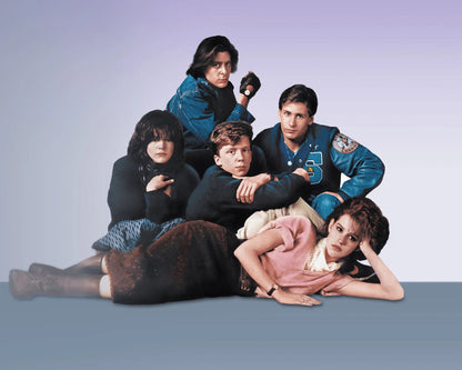 A group of five people posed together against a soft lavender-to-blue studio background. The scene appears to be a movie or TV still, with one person in a blue jacket at the top, two people in dark clothing in the center, and two people reclining at the bottom.