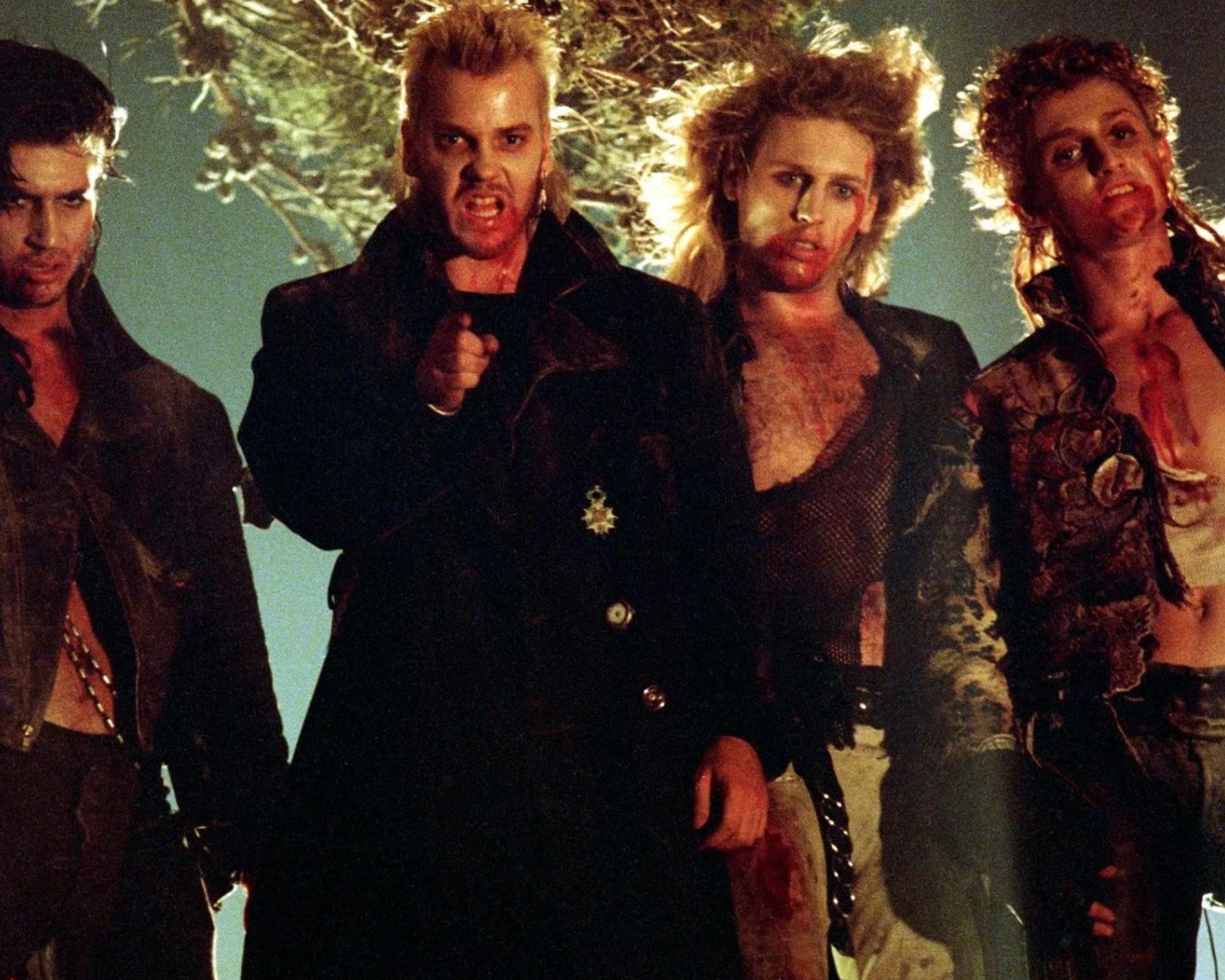 Four men in dark, distressed costumes standing together against a dim, greenish background with tree-like lighting effects.