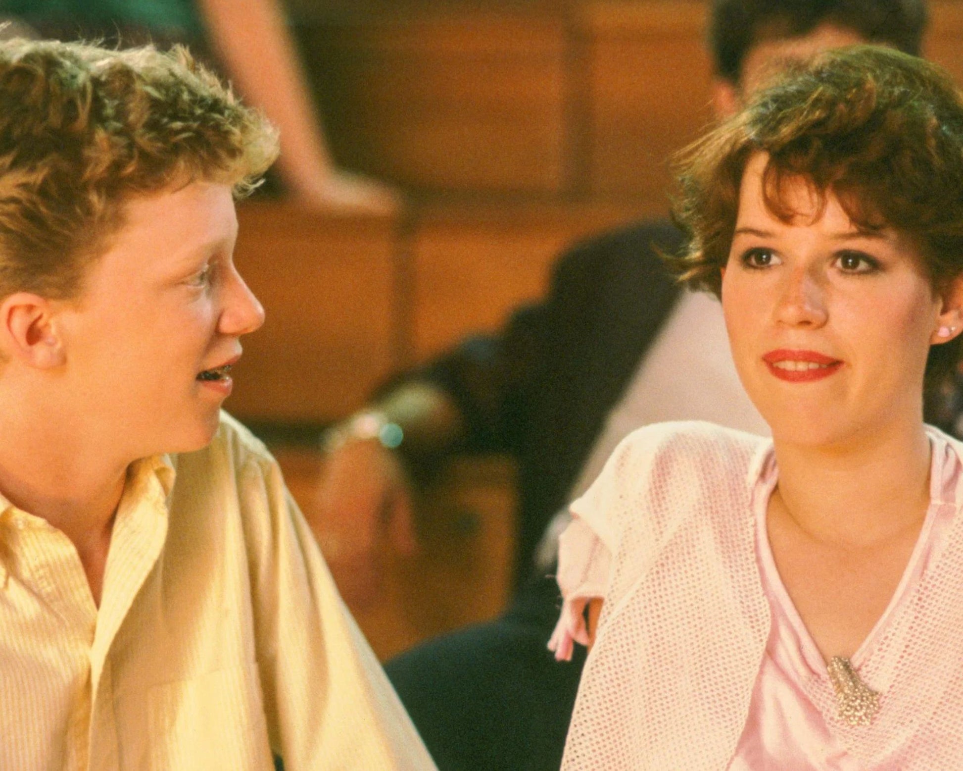 A close-up shot of a young man in a pale yellow striped shirt and a young woman in a light pink top, captured in a candid moment with a blurred background.