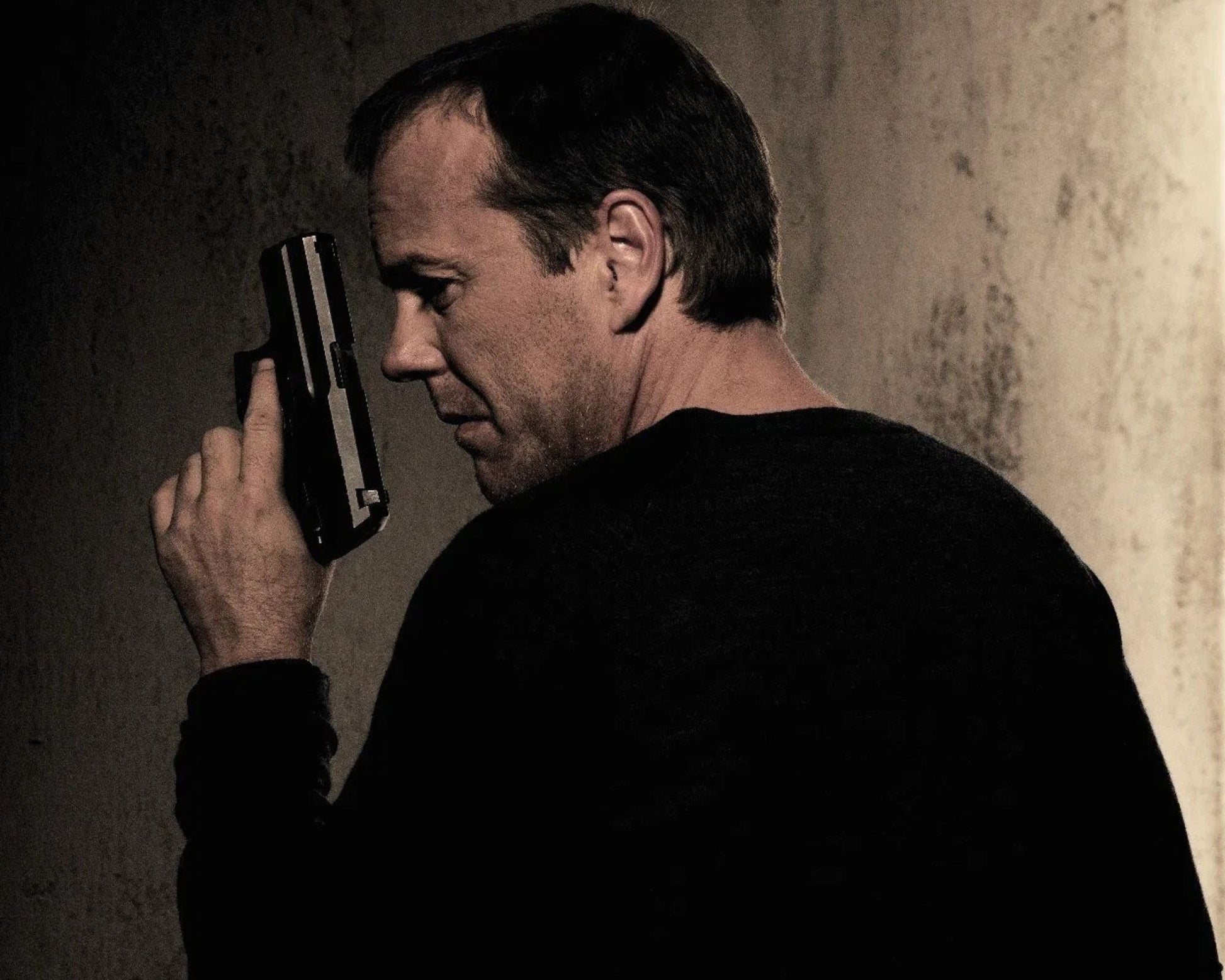 A man in a black long-sleeve shirt holding a handgun to his head, shown in a dramatic, high-contrast, sepia-toned scene against a textured wall.