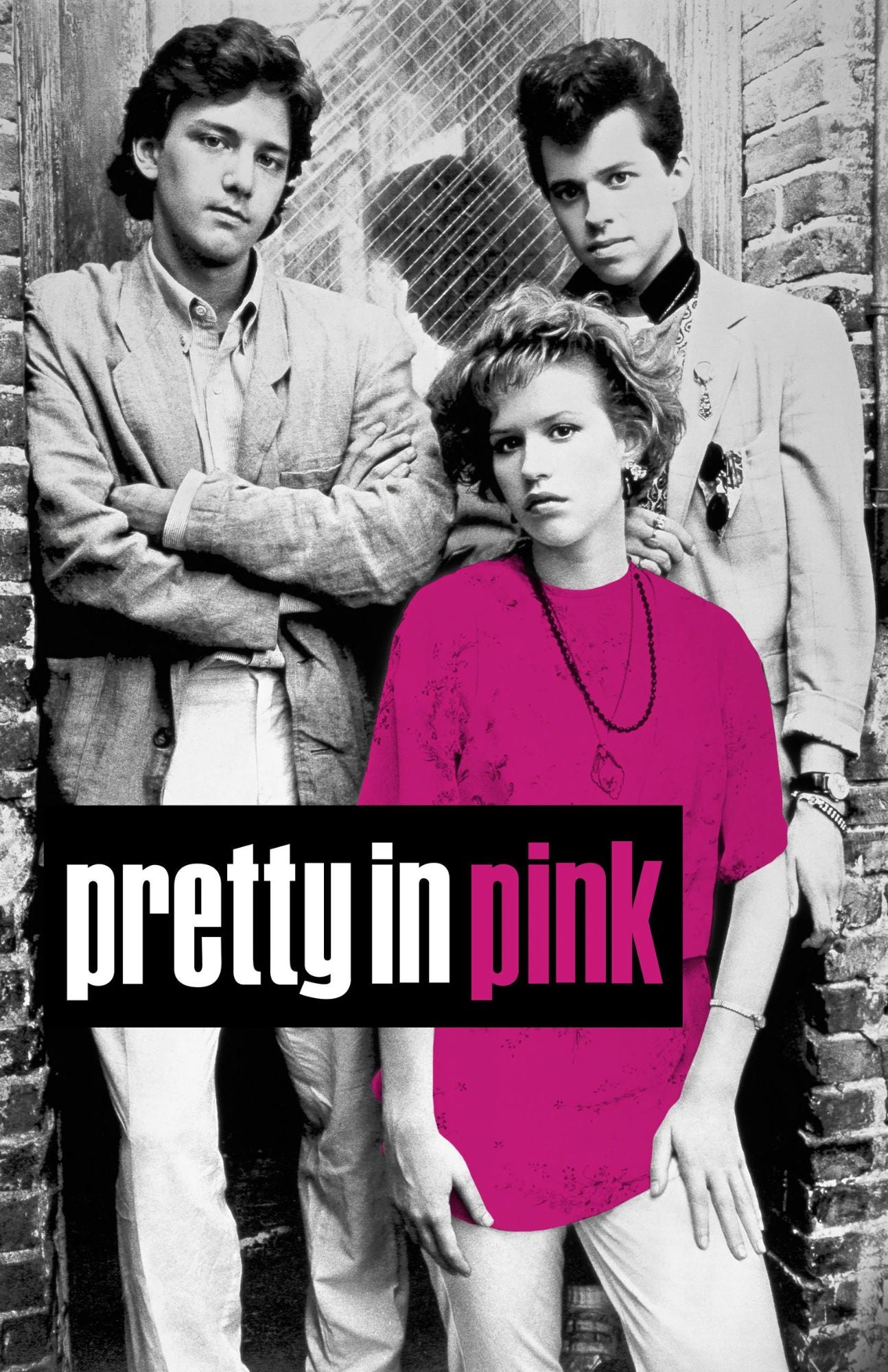 A stylized promotional photo of three people posed against a brick wall, with the title text 'pretty in pink' overlaid across the lower portion. The woman in the foreground wears a vivid pink top and light pants, while the two men behind her are rendered in grayscale.